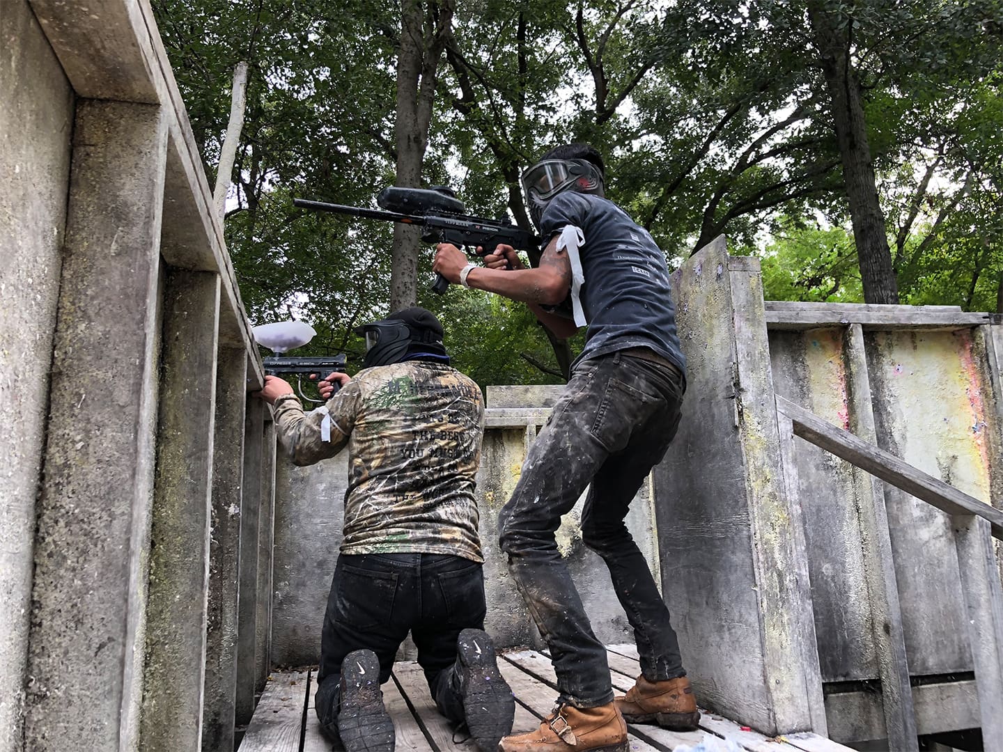 Two people in camouflage gear and helmets are playing paintball.