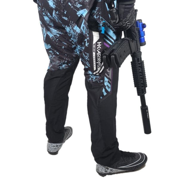 Person in paintball pants holding a paintball gun.