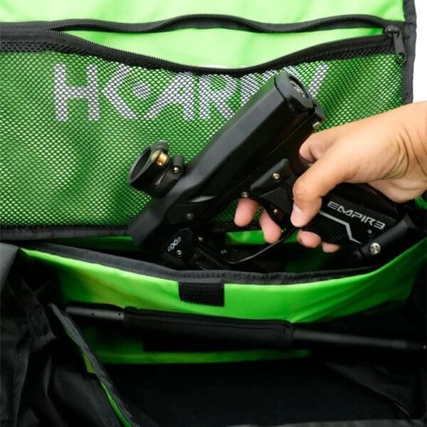 Hand holding paintball gun inside green bag.